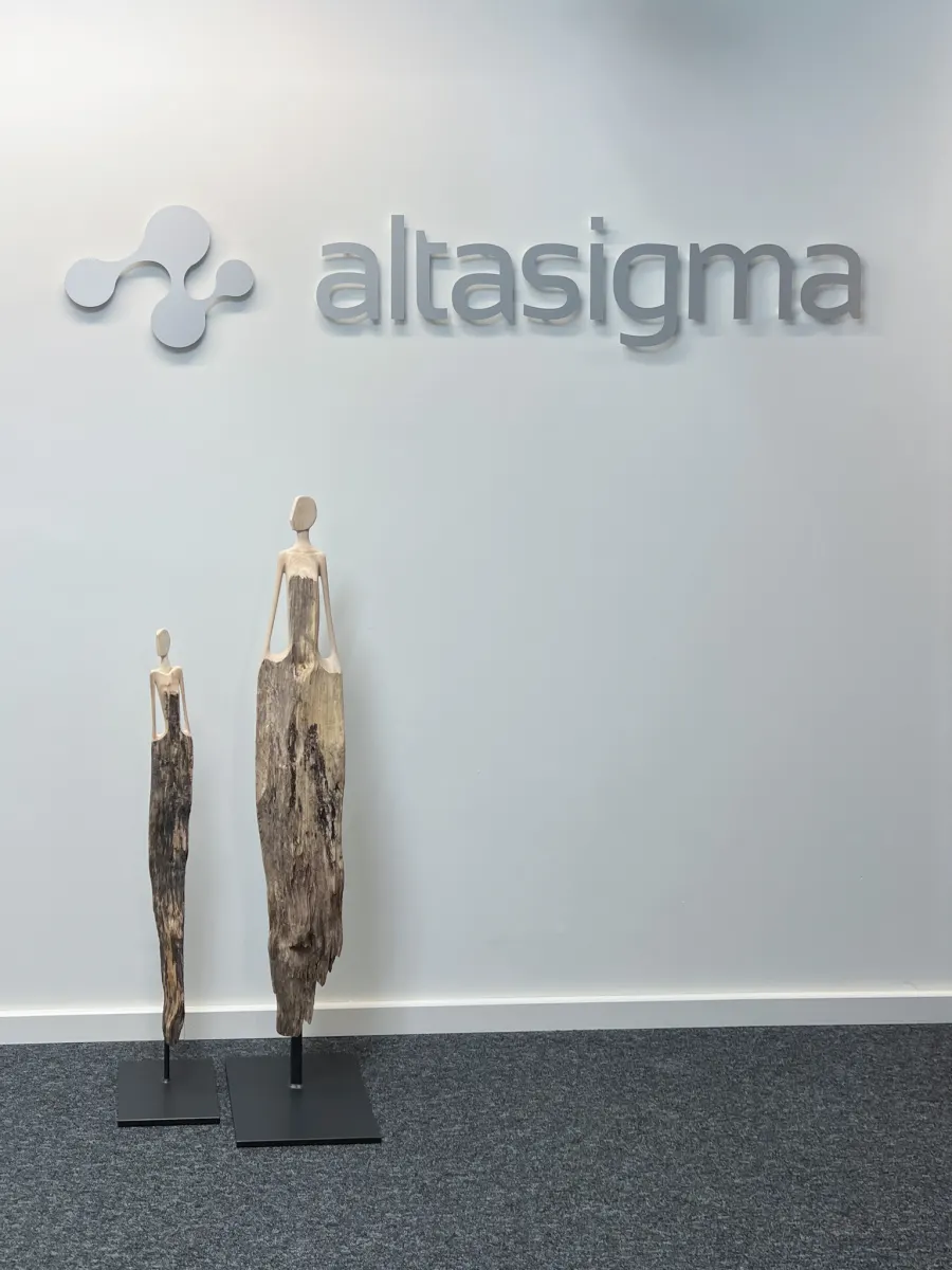 AltaSigma-Logo an der Bürowand mit zwei Holzskulpturen im Eingangsbereich